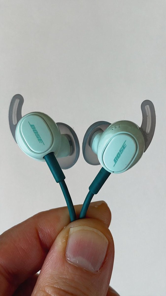 Mint Bose earbuds with wing tips held between fingers