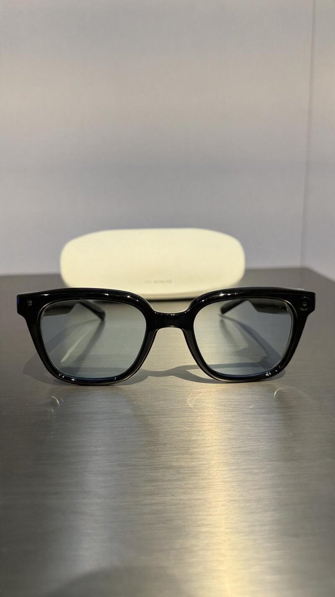 The black smart glasses on a metallic table, charging case in the background