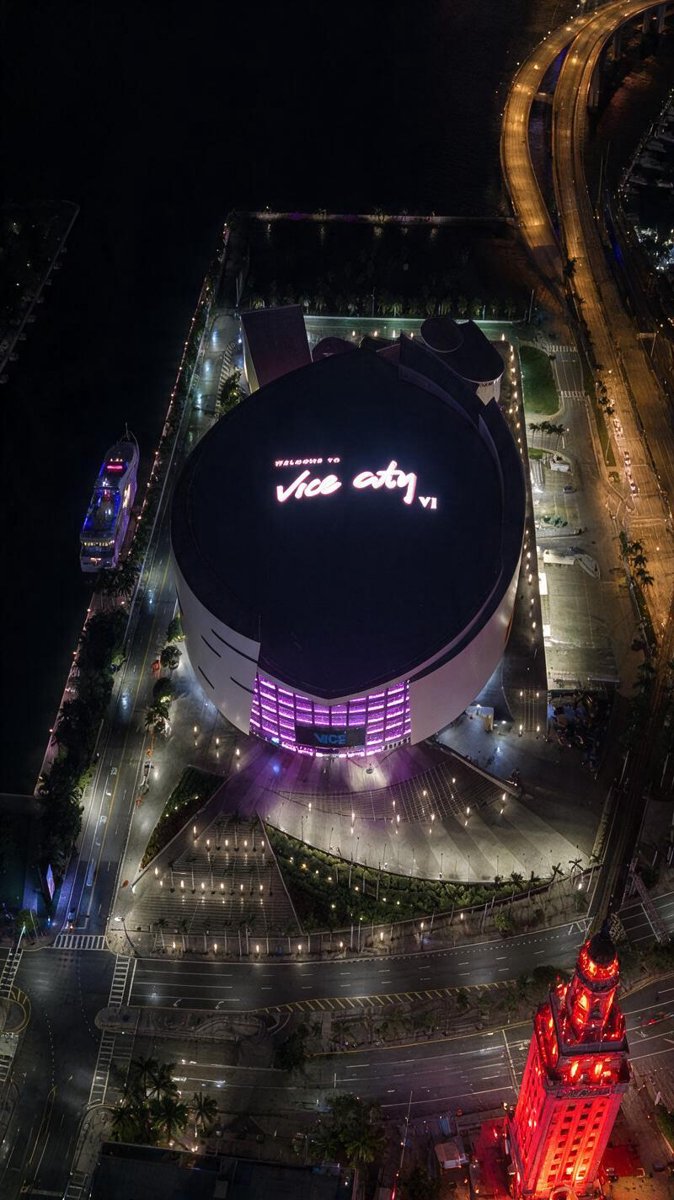 The arena glowing over the Miami waterfront — neon pink and teal washing across a real skyline