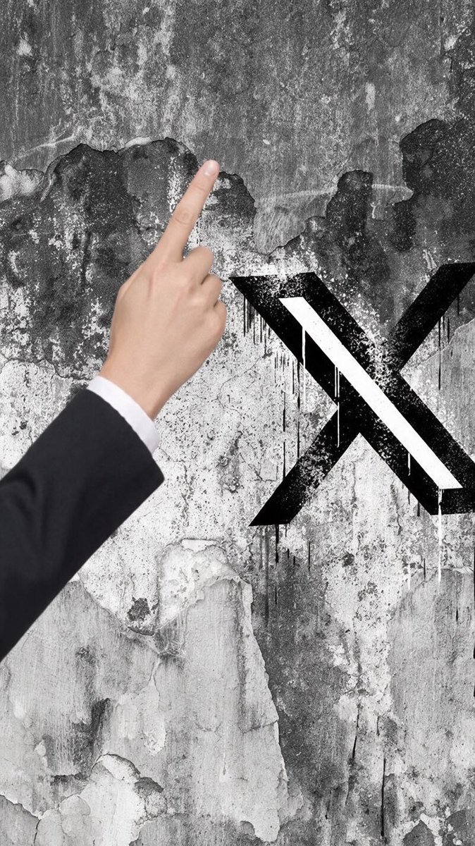 A hand pointing at an X logo painted on a weathered wall