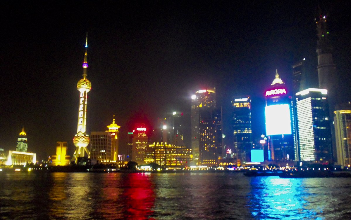 Real night photograph of the Shanghai Bund waterfront, with the Lujiazui skyline illuminated across the Huangpu river