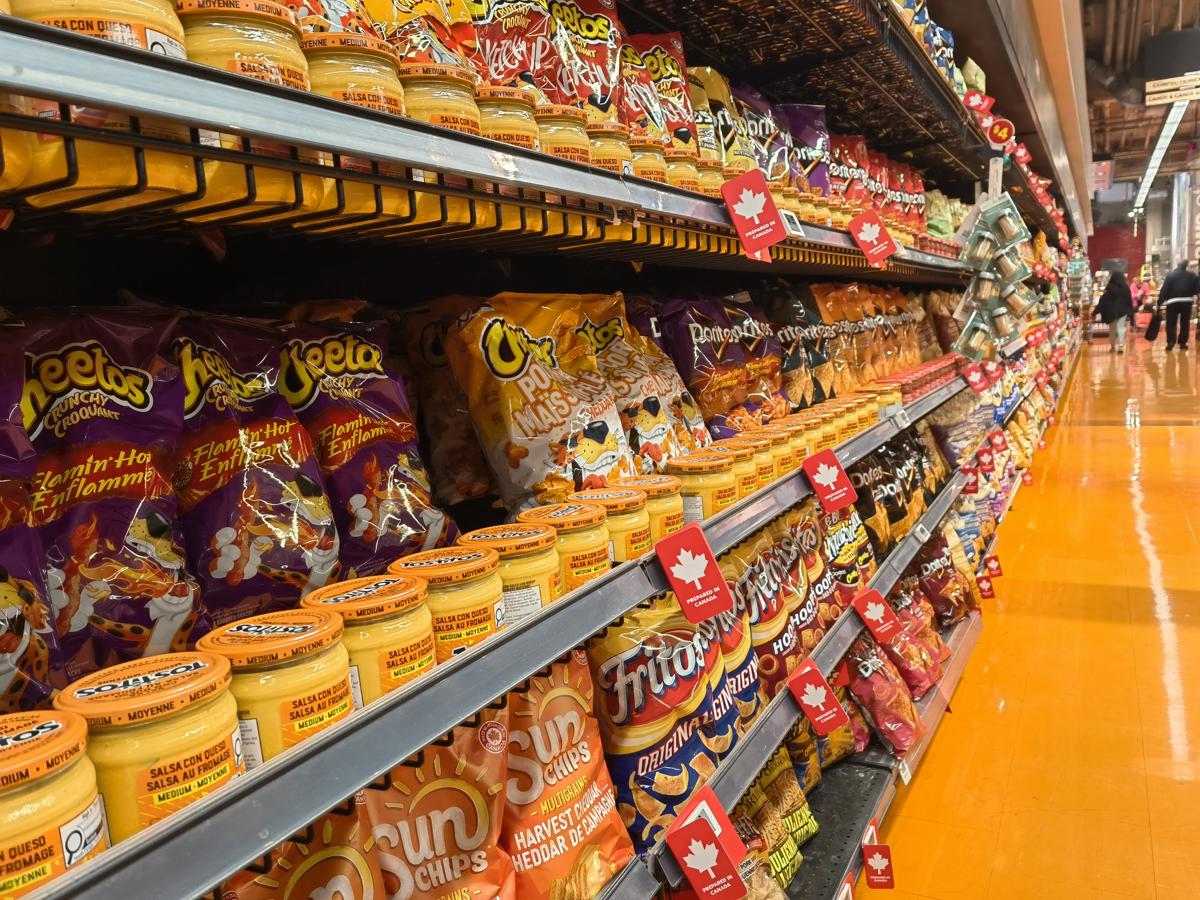 A Loblaws snack aisle with red maple-leaf shelf-edge tags marking Canadian products along the chip shelves