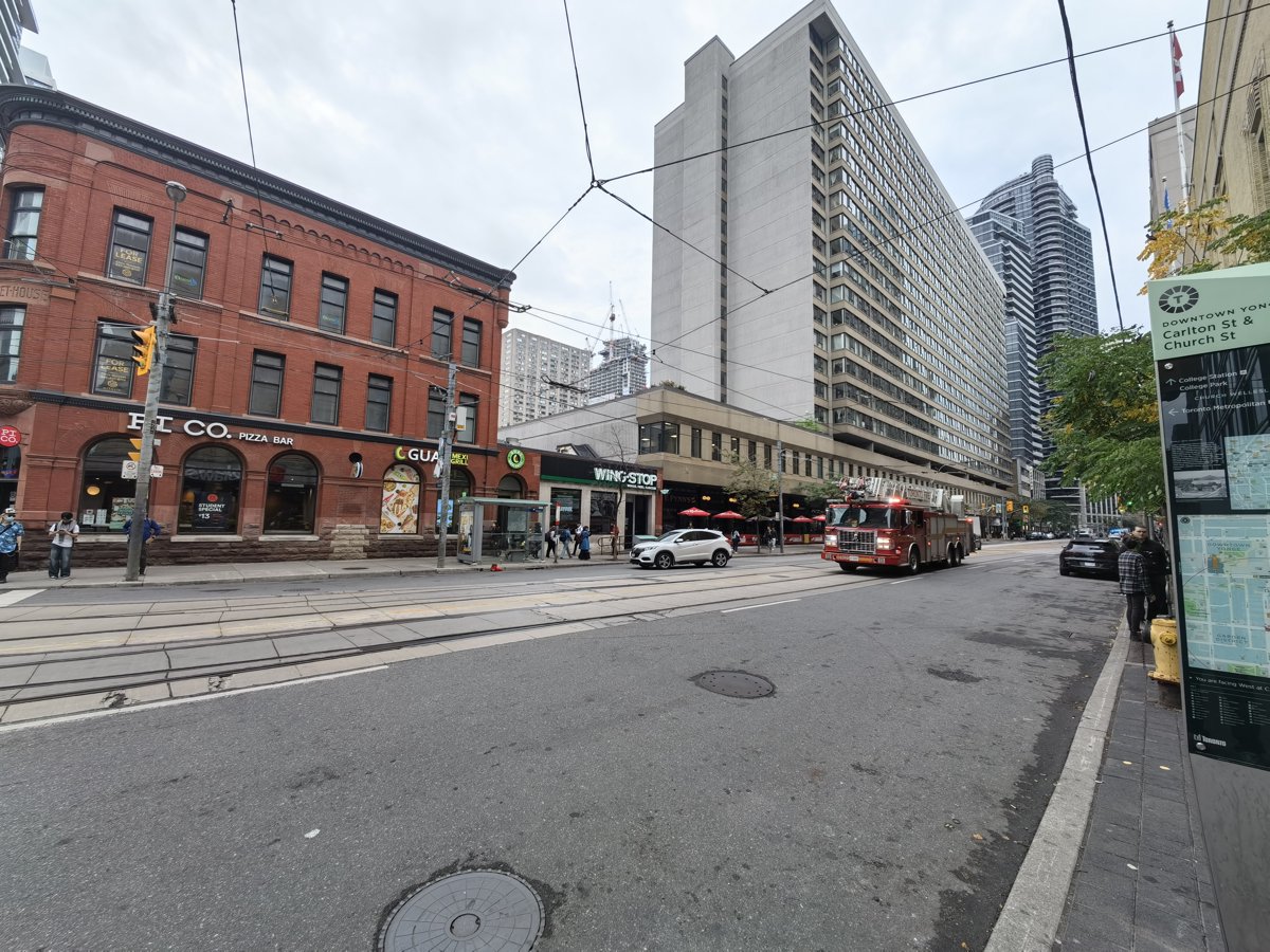 The corner of Carlton and Church in downtown Toronto, a Canadian flag flying near the wayfinding sign pointing to the Loblaws at Maple Leaf Gardens