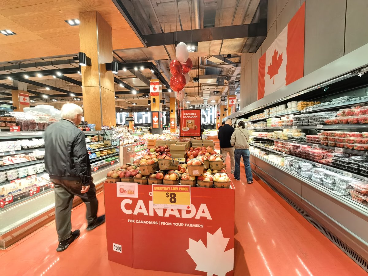 A Loblaws produce display wrapped in giant CANADA lettering under a Proudly Canadian banner, with flags and balloons above baskets of apples